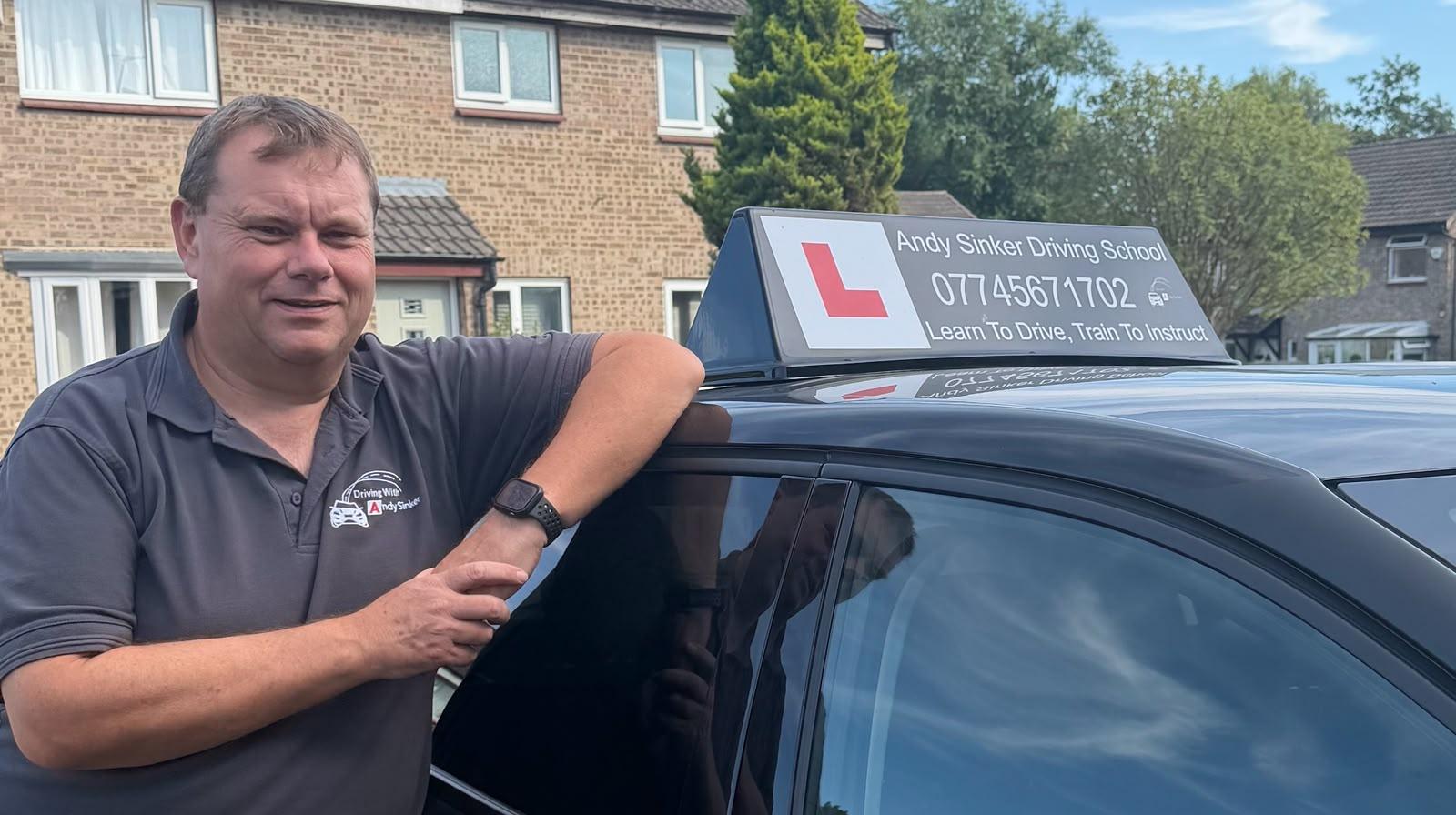 Andy Sinker leaning on his driving school car